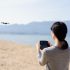 female-pilot-flying-drone-at-the-sandy-beach-of-the-lake-picture-id959507690